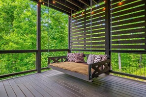 A wooden deck with a hanging swing seat, surrounded by a wooden fence with a lattice design. - New! 5BR cabin w/Hot Tub*Theater*Arcade*Fireplace (Pigeon Forge)