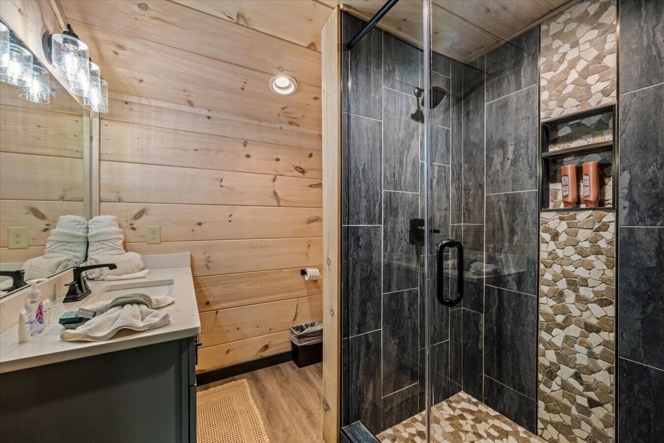 A bathroom with a wooden vanity, a glass shower enclosure, and a stone backsplash.