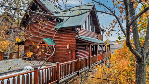 Eine Blockhütte mit Veranda und einem kleinen Anbau, umgeben von Herbstlaub.