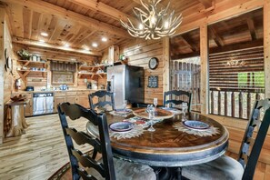 L’intérieur d’un chalet en bois comprend une salle à manger avec une table dressée pour quatre personnes, un coin cuisine et une grande fenêtre offrant une vue panoramique.