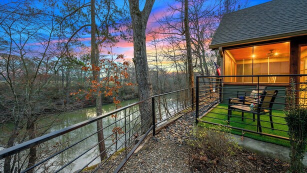Une vue sur la rivière, avec un chalet en bois, une rambarde en métal et un banc.