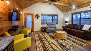 Un salon chaleureux avec des murs en bois, une cheminée, un canapé, un fauteuil et une table à manger.
