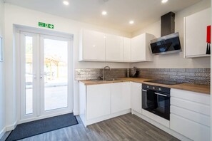 A modern kitchen with white cabinets, a stone backsplash, a stainless steel sink, a built-in oven, and a flat-screen TV.