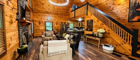 A log cabin interior with a living room, kitchen, and staircase.
