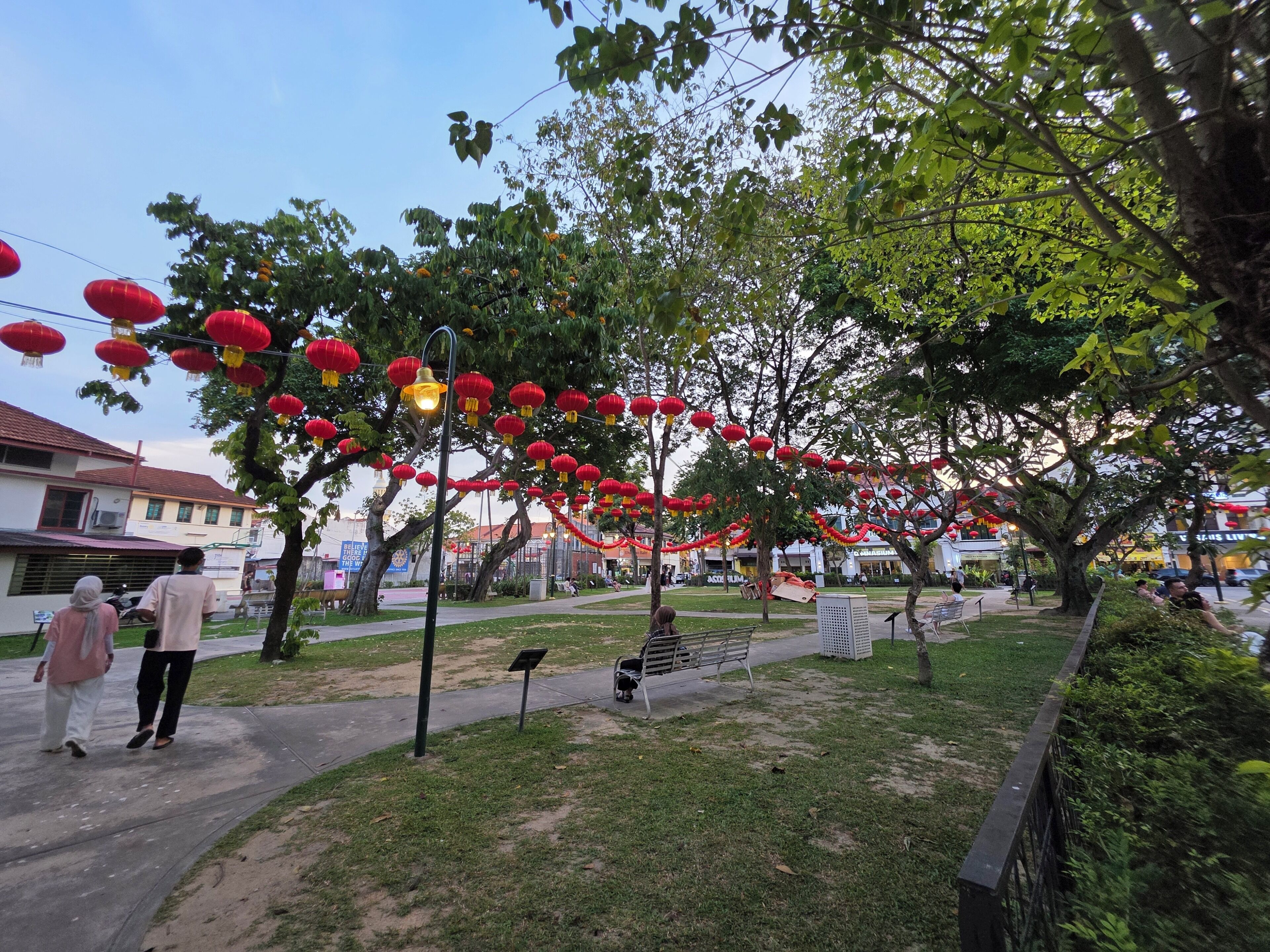 A park with trees, a pathway, and red lanterns.