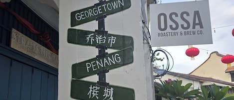 A directional signpost with multiple destination labels, a nearby building with a sign for OSSA Roastery & Brew Co., and a blue gate in the background.