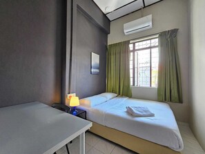 A room with a bed, a desk, an air conditioner, and a window with curtains. - Room at Lebuh Armenian Georgetown Penang (George Town)