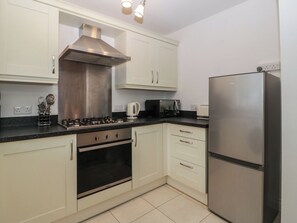 A kitchen with white cabinets, a stainless steel range, a microwave, a kettle, and a refrigerator. - 42 Ynys Y Nos (Neath)