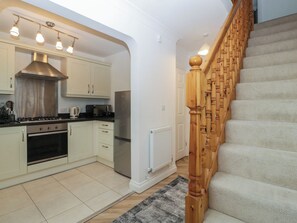 A modern kitchen with white cabinets, stainless steel appliances, and a wooden staircase. - 42 Ynys Y Nos (Neath)