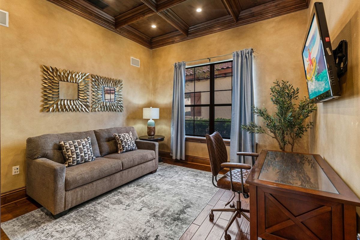 A living room with a sofa, a coffee table, a chair, a TV mounted on the wall, and a window with curtains.
