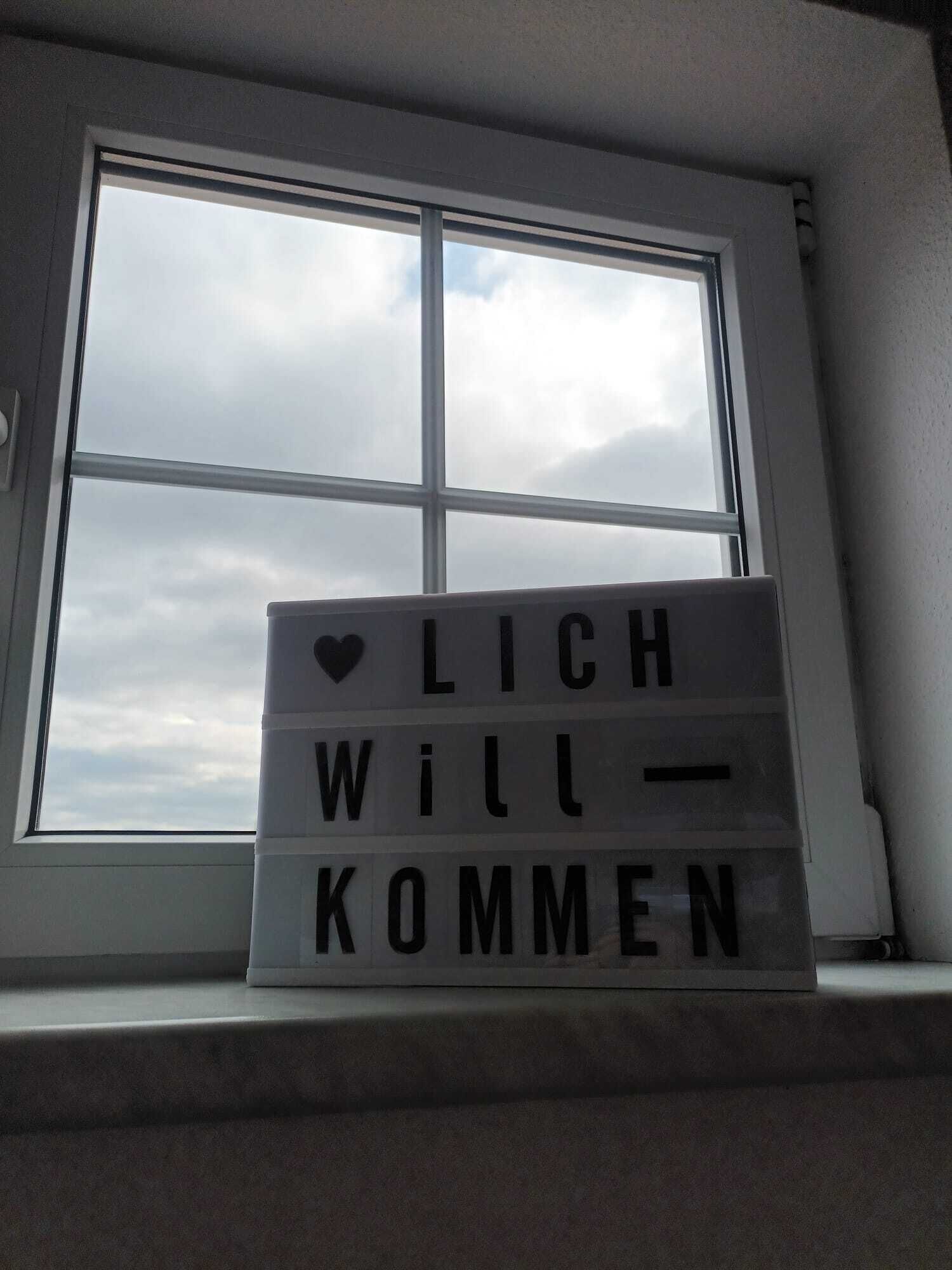 Una caja de luz con el texto 'LICH WILL KOMMEN' sobre un alféizar.