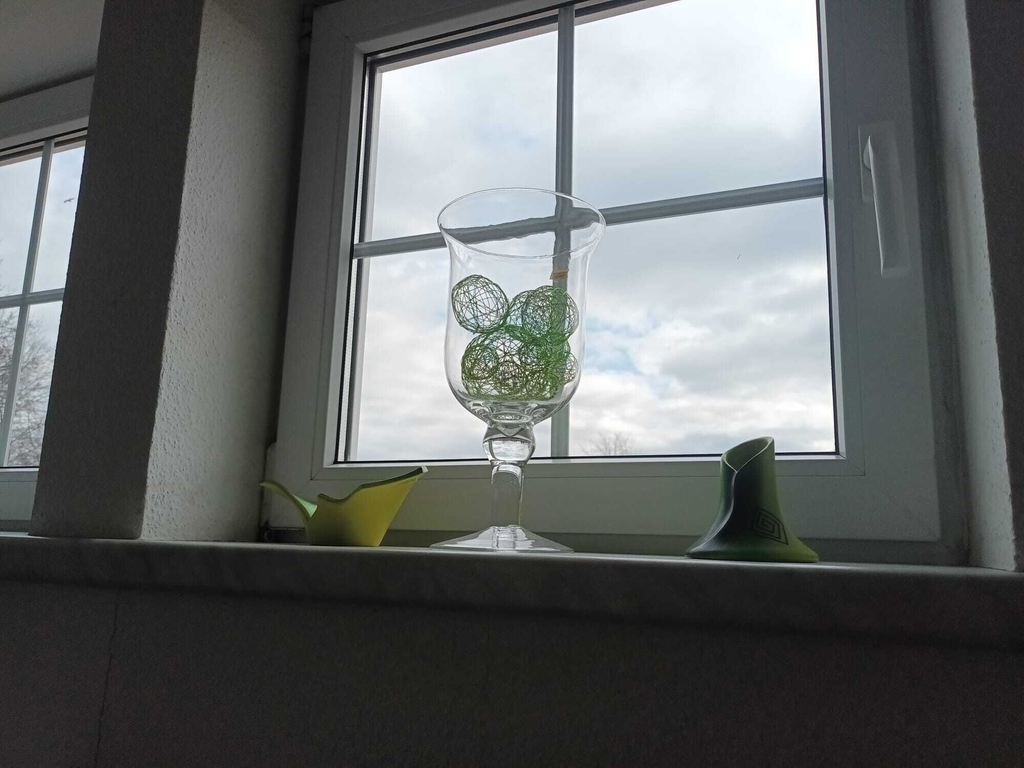 A clear glass vase with green spherical objects on a windowsill.