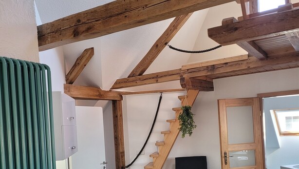 Une pièce avec un escalier en bois, une chaise noire, une porte en bois et un radiateur.