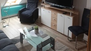 Un salon moderne avec un grand téléviseur à écran plat, un canapé, une table basse et un fauteuil.