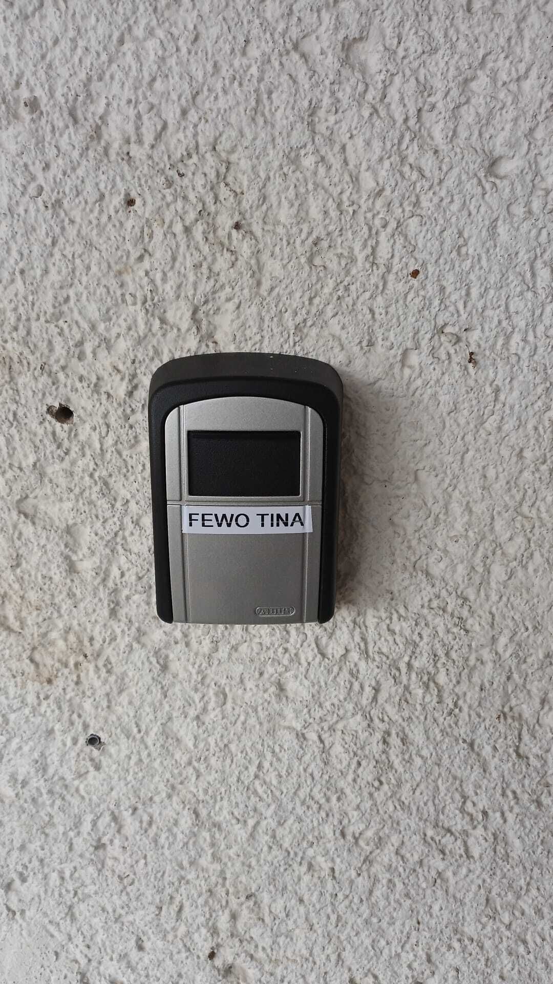 Ein kleines, rechteckiges Gerät mit der Aufschrift 'FEWO TINA' auf einer strukturierten Oberfläche.