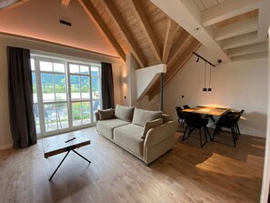 Un ampio soggiorno con divano, tavolo da pranzo e sedie, una grande finestra con vista e travi a vista al soffitto.