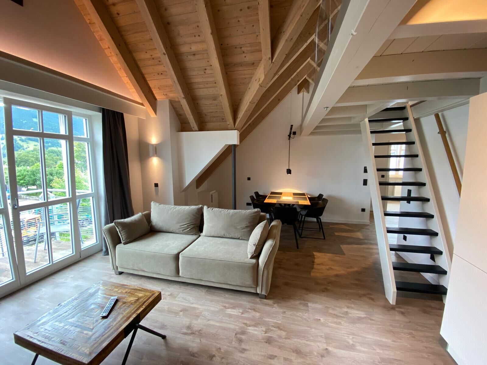 Ein modernes Wohnzimmer mit einer Couch, einem Holztisch, einem Esstisch mit Stühlen und einer Treppe.