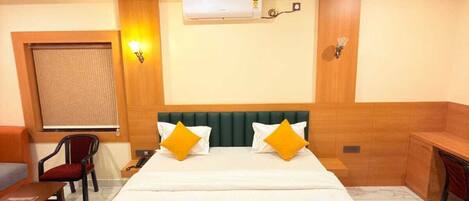 A hotel room with a bed, a desk, a chair, an air conditioning unit, and a ceiling fan.