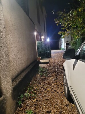 A narrow driveway leading to a building with a gated entrance, a white car parked on the right, and a small garden area with potted plants. - Matos's Vacation Rental. 3-bedroom house for 10 people. Pets allowed (Cellettes)