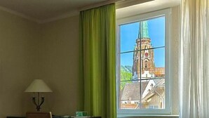 A hotel room with a bed, a desk, a chair, and a window with a view of a building. - Parkhotel Sonne (Schoenau im Schwarzwald)