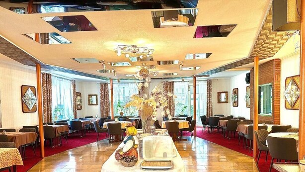 A spacious dining area with multiple tables and chairs, a central decorative piece, and a red carpet. - Parkhotel Sonne (Schoenau im Schwarzwald)