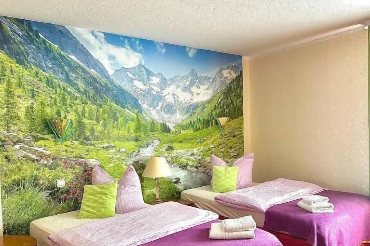A hotel room with two beds, a mountain landscape mural, a red carpet, and a ceiling light.
