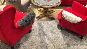 Un hall d’hôtel avec un mur en pierre, une cheminée, des canapés rouges, une table basse ronde et des tableaux.