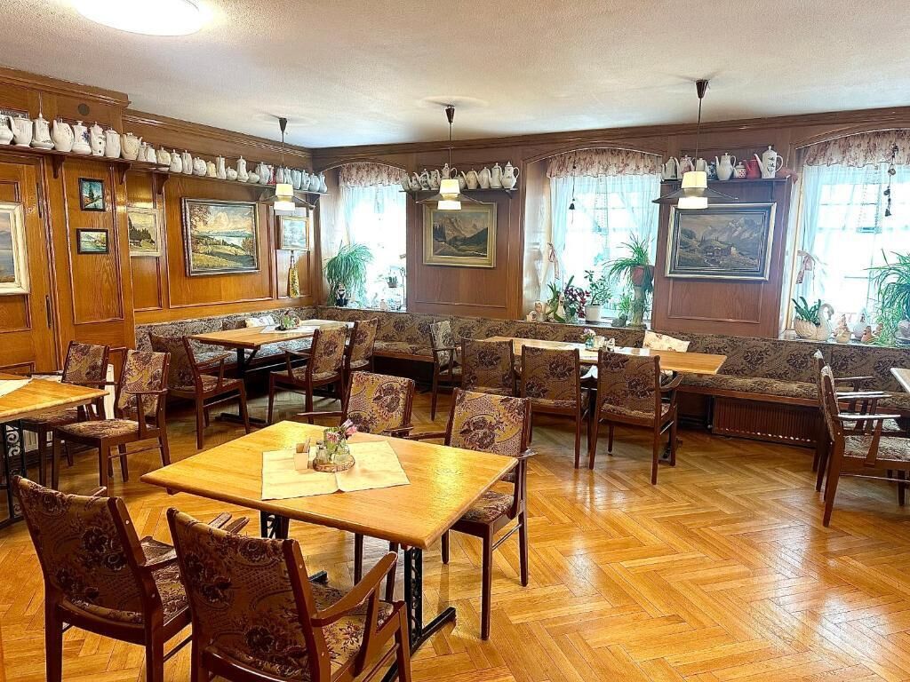 Un espace repas avec des tables et des chaises en bois, des œuvres d’art encadrées aux murs et des plantes en pot.
