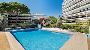 A swimming pool surrounded by greenery and modern buildings. - Air-conditioned studio with sea view and pool (Antibes)