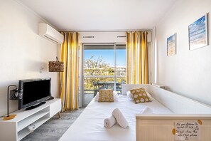 Een hotelkamer met een bed, een televisie, een balkon met gele gordijnen en een bord aan de muur.