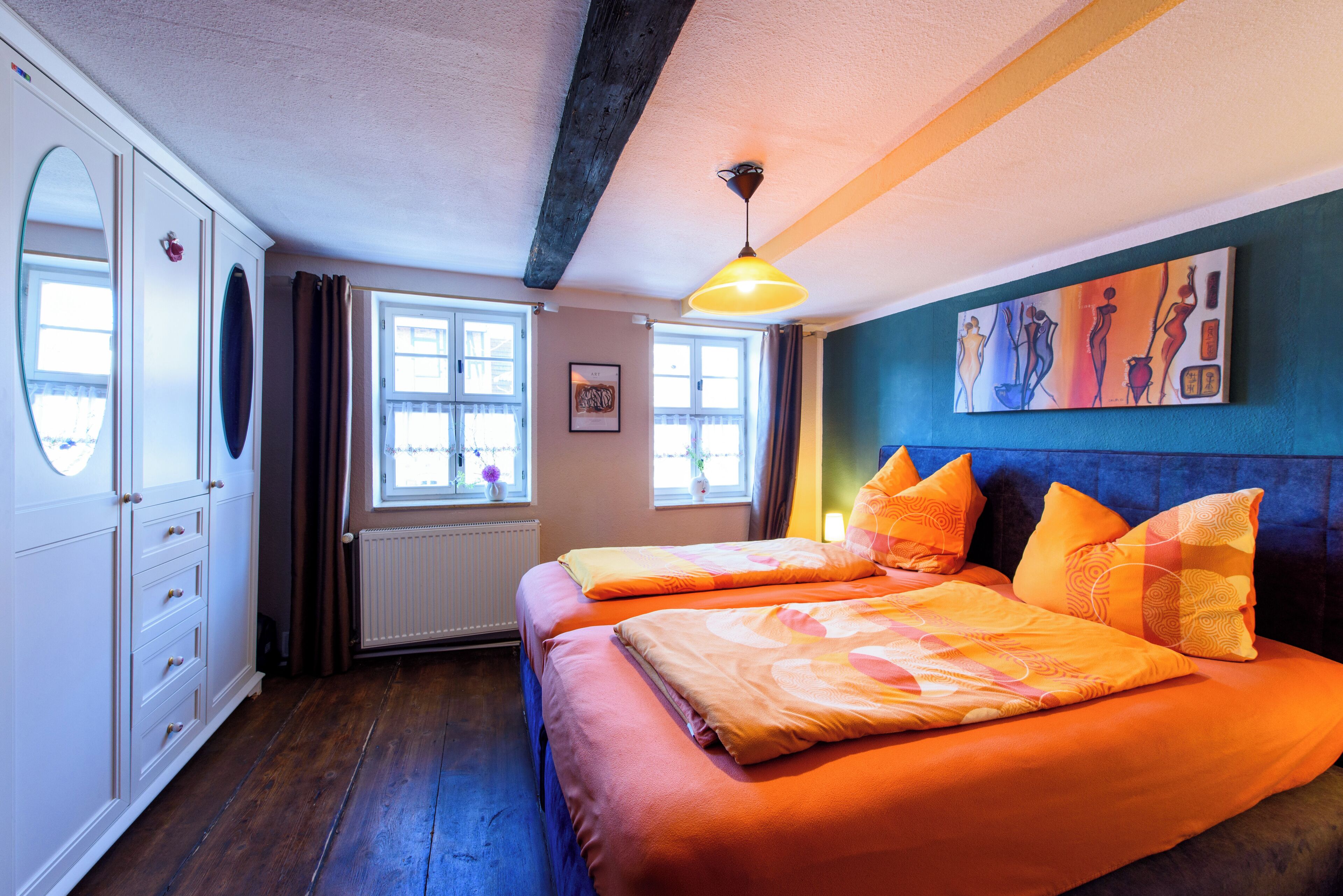 Ein Zimmer mit zwei Betten, einem Kleiderschrank, einem Heizkörper und einem Fenster mit Vorhängen.