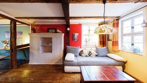 A cozy room with exposed wooden beams, a sofa with cushions, a wooden table, and a hanging lamp. - "Sunshine" in harmony and color (Quedlinburg)