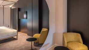 A modern bedroom with a large mirror, a bed, a TV, and two chairs. - Residenza Palazzo Poste (Verona)