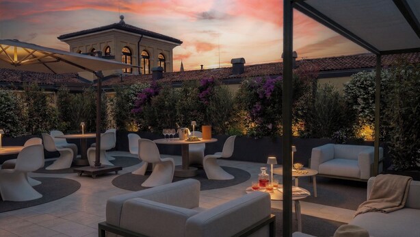An outdoor seating area with modern furniture, a table with drinks, and a building in the background. - Residenza Palazzo Poste (Verona)