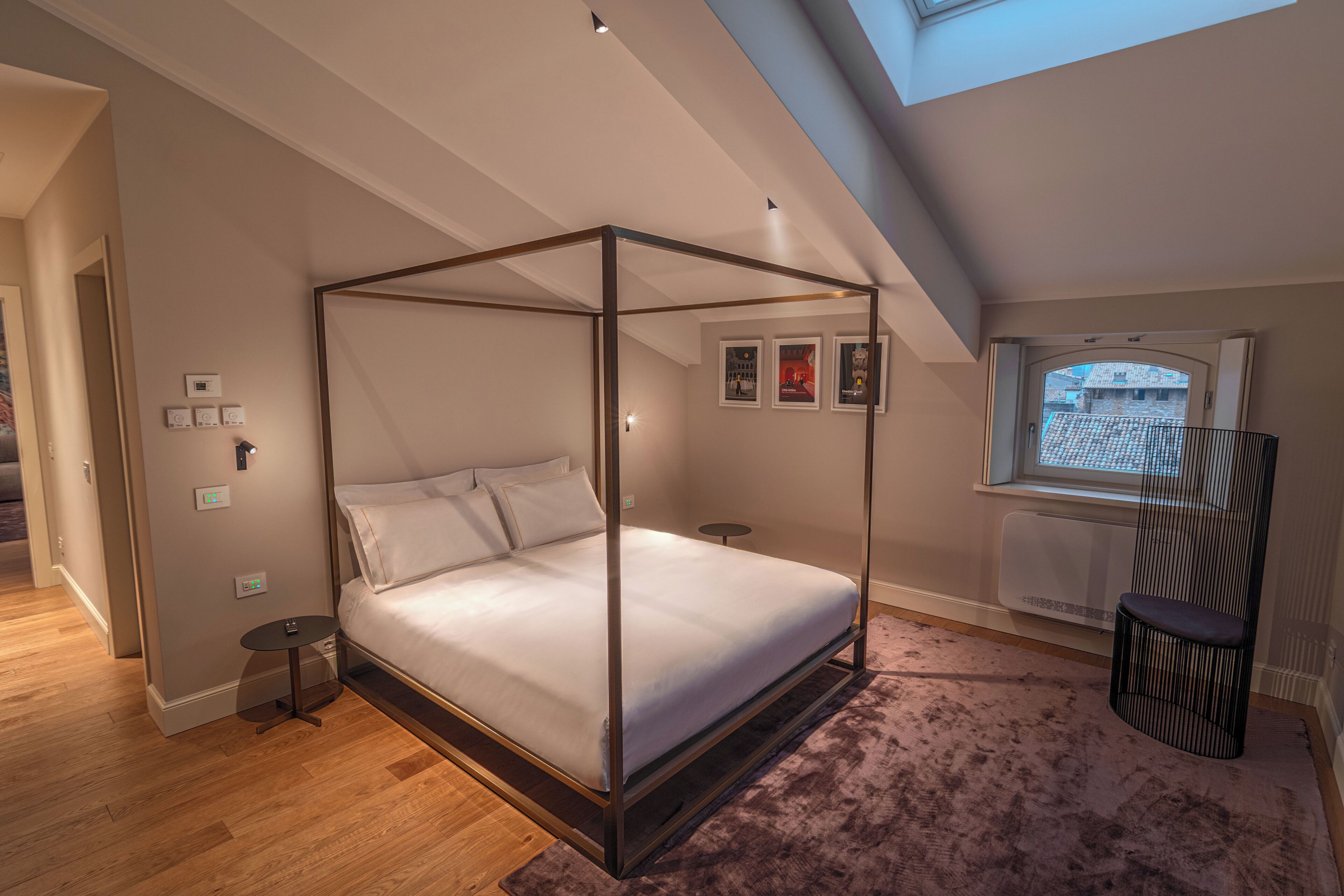 Ein Schlafzimmer mit Himmelbett, einem kleinen runden Tisch, einer Heizung und einem Fenster mit Blick auf Gebäude.