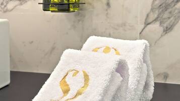 A bathroom with a marble wall, a yellow bottle of liquid soap, and two white towels with golden embroidery.
