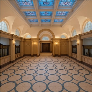 Un vaste hall doté d’un sol à motifs, de fenêtres en arc de cercle et d’une verrière ornée de vitraux.