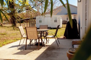Un patio con mesa y sillas, una parrilla y una casa rodante al fondo.