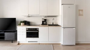A modern kitchen with white cabinets, a built-in oven, a coffee maker, and a refrigerator.