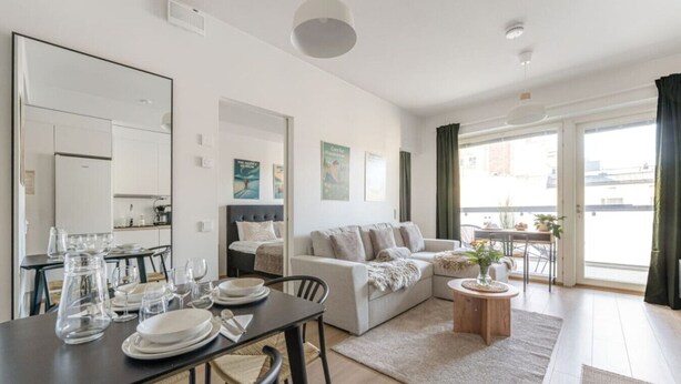 A modern living room with a dining area, a sofa, a small round table, and a balcony with a view.