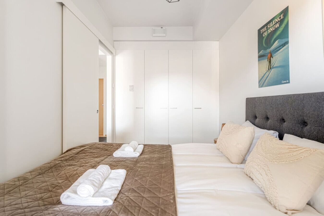 A hotel room with a bed, a bedside table, a poster on the wall, and a wardrobe.