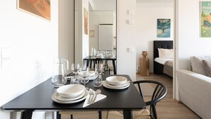 A dining area with a table set for four, a mirror, a bed with a headboard, and a poster on the wall.