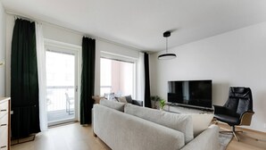A modern living room with a sofa, a TV, a chair, and a balcony with curtains. - Superior family room for 5 guests - Private Sauna (Tampere)