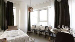 A hotel room with a bed, seating area, dining table, and large windows. - Nokia Arena By Come in! Deluxe Family Room (Tampere)