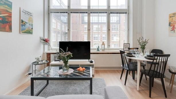 A modern living room with a large window, a flat-screen TV, a dining area with chairs, and a coffee table with decorative items. - Come in! `Värjäri` Parvellinen asunto Pyynikillä (Tampere)