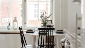 A dining area with a table set for two, a window with a view of buildings, and a radiator below the window. - Come in! `Värjäri` Parvellinen asunto Pyynikillä (Tampere)