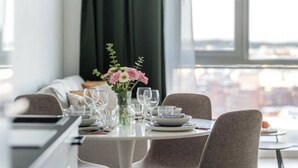 A dining area with a table set for four, a vase with flowers, and a city view through the window. - Arena Comfort Queen-Free Gym-Views (Tampere)