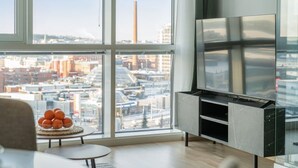 A modern living room with a large window, a flat-screen TV, and a small table with oranges. - Arena Comfort Queen-Free Gym-Views (Tampere)
