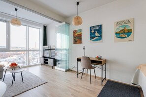 A modern living room with a large window, a glass partition, a desk, a chair, and artwork on the wall. - Arena Comfort Queen-Free Gym-Views (Tampere)