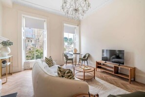 A modern living room with a sofa, television, and large windows. - Charming Apartment Steps from Bath Abbey - VAT Q (Bath)